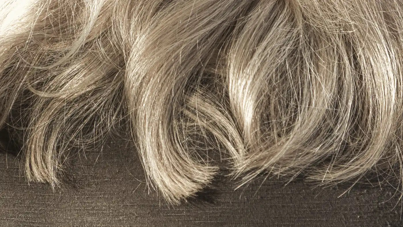 Löst hår i mjuka vågor utlagt på ett ljust tyg, utan träns eller fäste